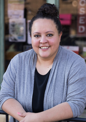Photo of Melanie resting arms on railing in front of retail storefront.